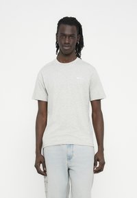 Light gray cotton t-shirt with short sleeves, round neckline, and a small logo on the left side. Worn with light blue denim jeans.