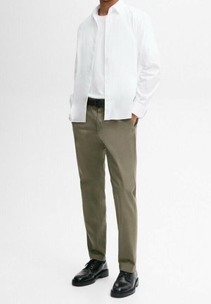 White long-sleeve shirt over a white t-shirt, paired with olive green trousers and black shoes. Smooth fabric, casual fit, no visible patterns.