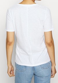 Weißes T-Shirt mit kurzen Ärmeln und Rundhalsausschnitt, aus leichtem Stoff. Hat einen geraden Schnitt und eine subtile Textur mit sichtbaren Nähten.