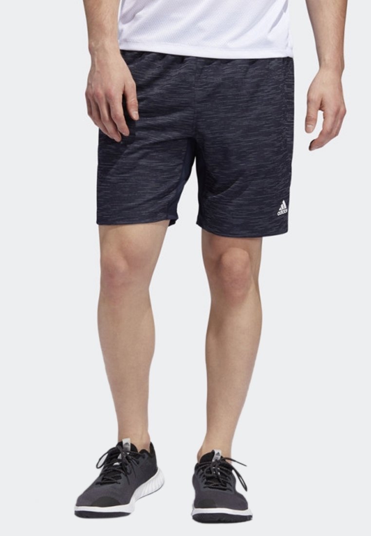 Homme portant un short de sport noir avec un motif discret et un logo Adidas blanc, associé à des chaussures de course noires et une chemise blanche.