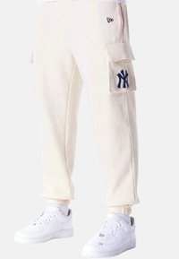 Beige cargo bukser med ribbede manchetter, med et marineblåt broderet logo på sidelommen. Sæt sammen med hvide sneakers.