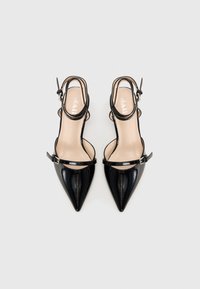 Décolleté in pelle laccata nera, con punta affusolata, cinturini alla caviglia e una soletta beige con testo argentato.