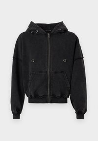 Crna zip-jakna od mekanog materijala. Ima kapuljaču s metalnim detaljima, prednje džepove i nabranice na rukavima i rubu.