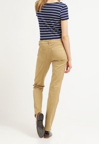 Světlé béžové kalhoty se zúženým střihem, pěti kapsami a hladkou texturou, doplněné námořnickou pruhovanou košilí s krátkým rukávem.