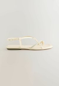 Sandalini flat color avorio con sottili cinturini lucidi e un accento di strass sulla punta. Presentano una fibbia regolabile per una vestibilità ottimale.