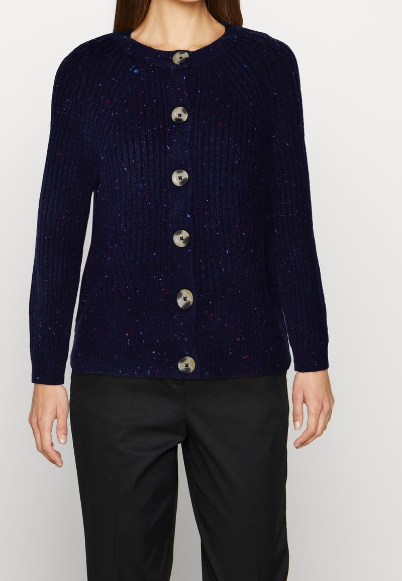 Marinblå ribbad cardigan med flerfärgade prickar, med sex stora runda knappar fram och långa ärmar. Slät stickad textur.