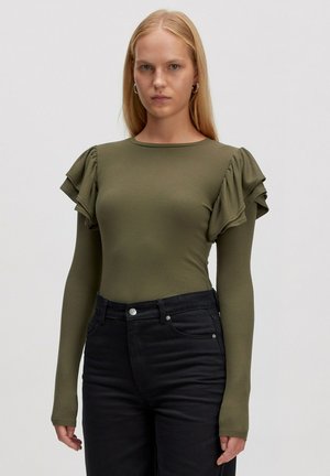 Olivgrünes, geripptes Langarmoberteil mit gerafften kurzen Ärmeln, kombiniert mit schwarzen, eng anliegenden Jeans und einem silbernen Knopfdetail an der Taille.