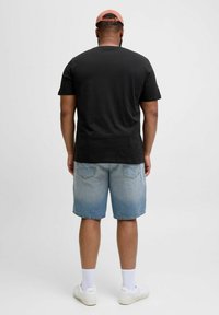 Juodas medvilnės marškinėliai trumpomis rankovėmis; derinami su šviesiai mėlynomis džinsinėmis šortais, turinčiais nudilimo efektą; baltos sportinės bateliai ir kojinės.