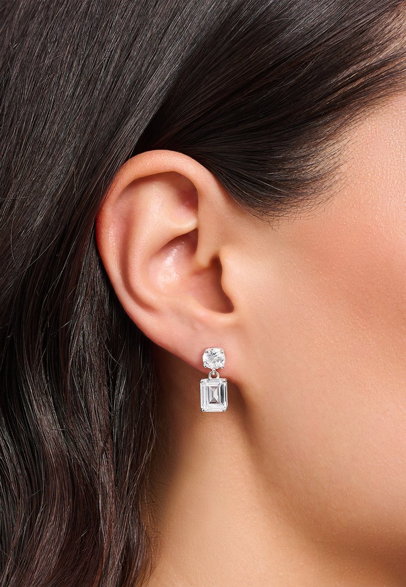 Silberne Drop-Ohrringe mit einem runden, klaren Edelstein oben und einem rechteckigen, klaren Edelstein darunter, die das Licht mit einer glatten Oberfläche reflektieren.