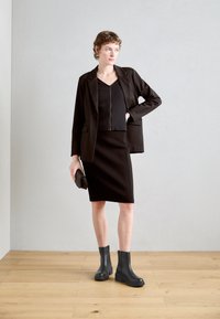 Blazer noir ajusté sur un haut et une jupe noir côtelé, assorti de bottines noires à la cheville. Tissu lisse avec un design structuré et des accents minimaux.