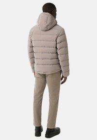 Puffer jacket in light beige with horizontal quilted design, attached hood, and zip closure. Paired with beige pants and black shoes.