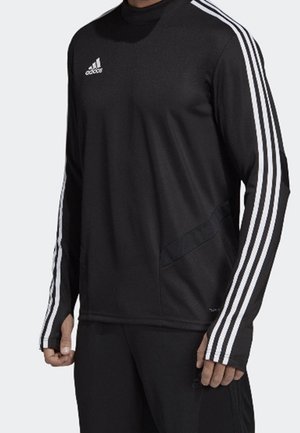 Homme portant un haut à manches longues noir Adidas avec trois bandes blanches sur les manches et un logo Adidas sur la poitrine.