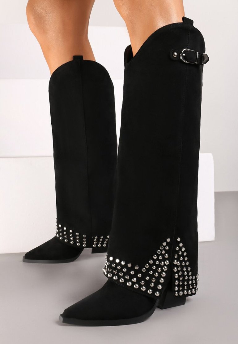 Bottes noires en daim hauteur genou avec un bout pointu, des accents cloutés à la base, et un détail de boucle sur le côté. Texture mate.