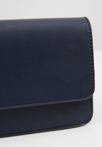Portafoglio in pelle blu navy con superficie liscia, forma rettangolare e cuciture a contrasto. Presenta una chiusura a pattina e un design minimalista.