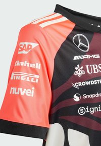 Camiseta deportiva roja y negra de manga corta. Presenta múltiples logotipos, incluidos SAP, Einhell, Pirelli y otros. Tejido texturizado y cuello de punto.