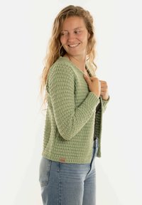 Groene gebreide cardigan met een gestructureerd patroon, v-hals en lange mouwen. Beschikt over een klein stoffen label aan de onderkant.