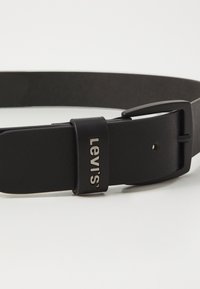 Black leather belt with a matte finish, featuring a silver metal buckle and a logo patch embossed near the buckle. Simple and streamlined design.