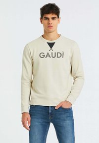 Felpa beige chiaro con scollatura tonda e maniche lunghe. Presenta la scritta nera "GAUDÌ" e un accento triangolare. Realizzata in morbido misto cotone.