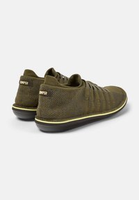 Dark green knit shoes with a soft, textured upper, elastic laces, and a slim black sole featuring a yellow accent around the edge.