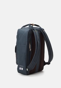 Mochila azul oscura hecha de tela con un respaldo acolchado y de malla texturizada. Cuenta con detalles en marrón, asa superior y bolsillo con cremallera lateral.