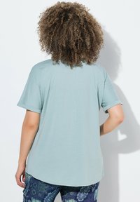 Světle modré tričko s krátkým rukávem, mírně oversize střih, měkký materiál, detail švu na zadní straně, spárované se vzorovanými tmavě modrými kalhotami.