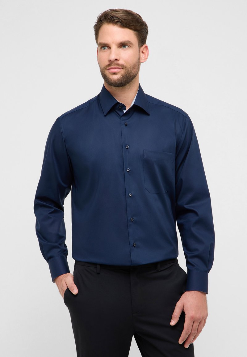 Chemise boutonnée à manches longues bleu marine en tissu lisse, avec une poche poitrine, un col intérieur contrastant et des boutons noirs.