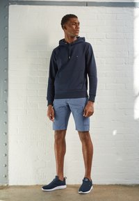 Námořnická mikina s přední kapsou, kombinovaná se světle modrými cargo šortkami a námořnickými teniskami, s texturovaným povrchem a volným střihem.