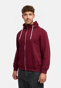 Bordowy rozpinany hoodie wykonany z miękkiego materiału, z kapturem, dwoma przednimi kieszeniami oraz kontrastowymi białymi sznurkami.