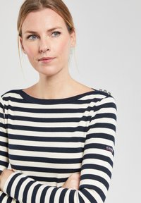 Maglione a righe blu navy e bianche con maniche lunghe realizzato in materiale morbido, dotato di scollo a barca e bottoni decorativi sulla spalla.