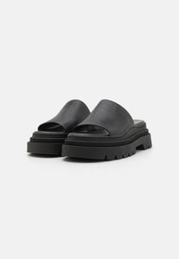 Černé kožené šlapky mají otevřenou špičku a silnou, rýhovanou gumovou podrážku s robustním designem. Hladký povrch a minimalistický styl.
