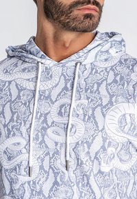 Felpa con cappuccio in blu chiaro, caratterizzata da un motivo a stampa serpente, cordini e dettagli in metallo argentato. Tessuto dalla consistenza morbida.