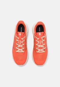 Orange athletic shoes with mesh upper, beige laces, and 'Salomon' branding. Features a textured surface and a cushioned white sole.
