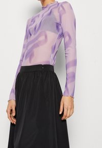 Durchsichtige lila Bluse mit langen Ärmeln, abstraktem Muster und Rüschenausschnitt, kombiniert mit einem schwarzen Rock mit gerafftem Taillenbund und Reißverschluss.