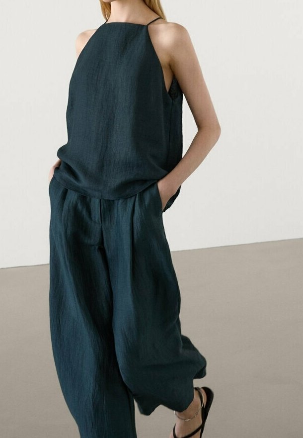 Haut sans manches en vert foncé avec de fines bretelles, associé à un pantalon large et ample. Le tissu a une texture douce, créant une silhouette décontractée.
