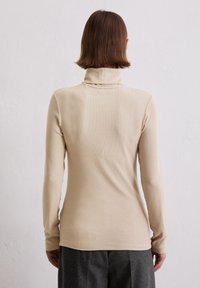 Beige Langarm-Turtleneck-Oberteil mit glatter Textur und figurbetontem Design, kombiniert mit grauen Hosen. Schlichte und moderne Ästhetik.