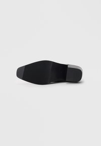 Suela de zapato de cuero negro con un patrón de agarre texturizado, forma ligeramente cónica y un acento gris en el talón.