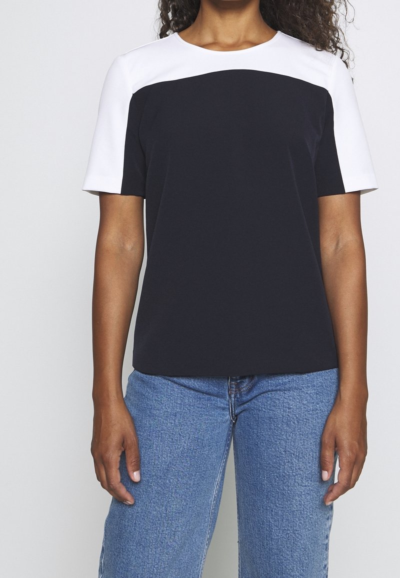 T-shirt a blocchi di colore bianco e nero con maniche corte, scollo rotondo e tessuto morbido. Abbinato a denim azzurro chiaro.