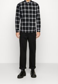 Koszula w czarno-białą kratę z długimi rękawami i zapięciem na guziki, w połączeniu z podwiniętymi czarnymi spodniami i czarnymi botkami na kostkę.