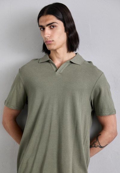 Polo shirt vert à manches courtes avec un col en V, fabriqué en tissu texturé. Conçu avec une coupe décontractée et présente des détails de couture subtils.