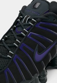 Κοντινό πλάνο μαύρου και μωβ Nike Shox αθλητικού παπουτσιού με λεπτομερή κορδόνια, δίκτυο στο επάνω μέρος και ορατή κουρτίνα. 