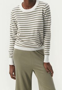 Pull à manches longues rayé en beige doux et blanc, avec un col rond, des poignets côtelés et une coupe décontractée. Associé à un pantalon vert olive.