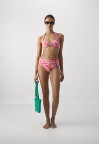 Floralni bikini u ružičastim i narančastim tonovima, s uvijenim bandeau gornjim dijelom i visokim donjim dijelom. Dodaci uključuju teksturiranu zelenu torbicu.