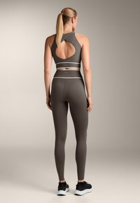 Magas nyakú sportmelltartó és illeszkedő leggings sötétszürke anyagból, nyitott hátrésszel, fehér részletekkel és testhez simuló szabással.