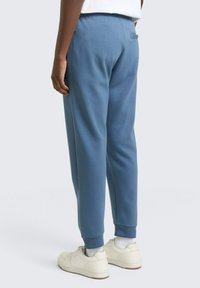 Jasnoniebieskie spodnie dresowe o zwężanych nogawkach wykonane z miękkiego materiału, z elastycznym paskiem w talii, prążkowanymi ściągaczami oraz jedną tylną kieszenią. Założone białe trampki.