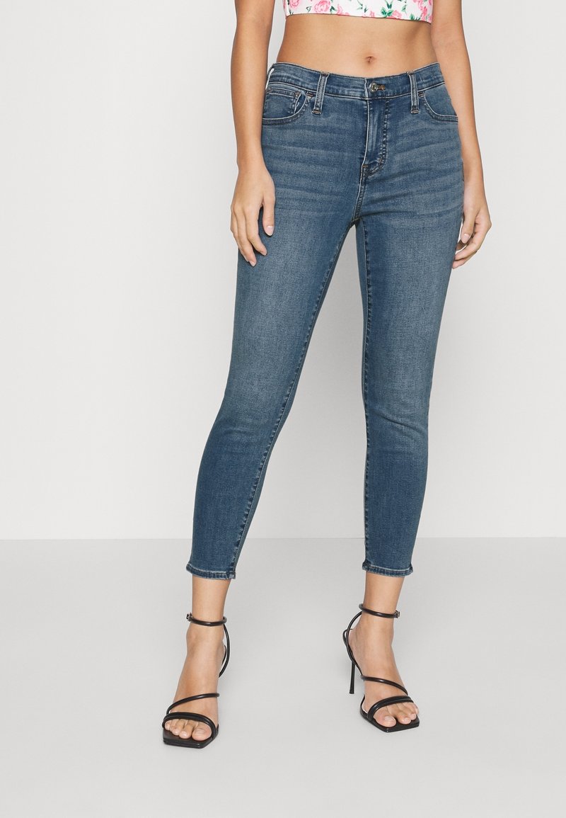 Skräddarsydda mörkblå denimjeans med en slät textur, femfickorsdesign, medelhög midja och avkortad längd, kombinerade med svarta högklackade sandaler.