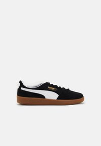 Baskets en daim noir avec accents en cuir blanc et semelle en caoutchouc marron. Présentent le logo Puma et la marque Palermo sur le côté. Design classique à tige basse.