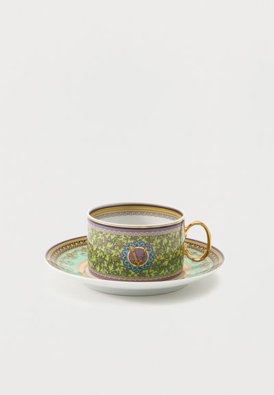 Κούπα τσαγιού και πιατάκι με περίτεχνα στολίδια σε πράσινο, μοβ και χρυσό χρώμα και λαβή της κούπας σε χρυσό, τοποθετημένα πάνω σε λευκό φόντο.