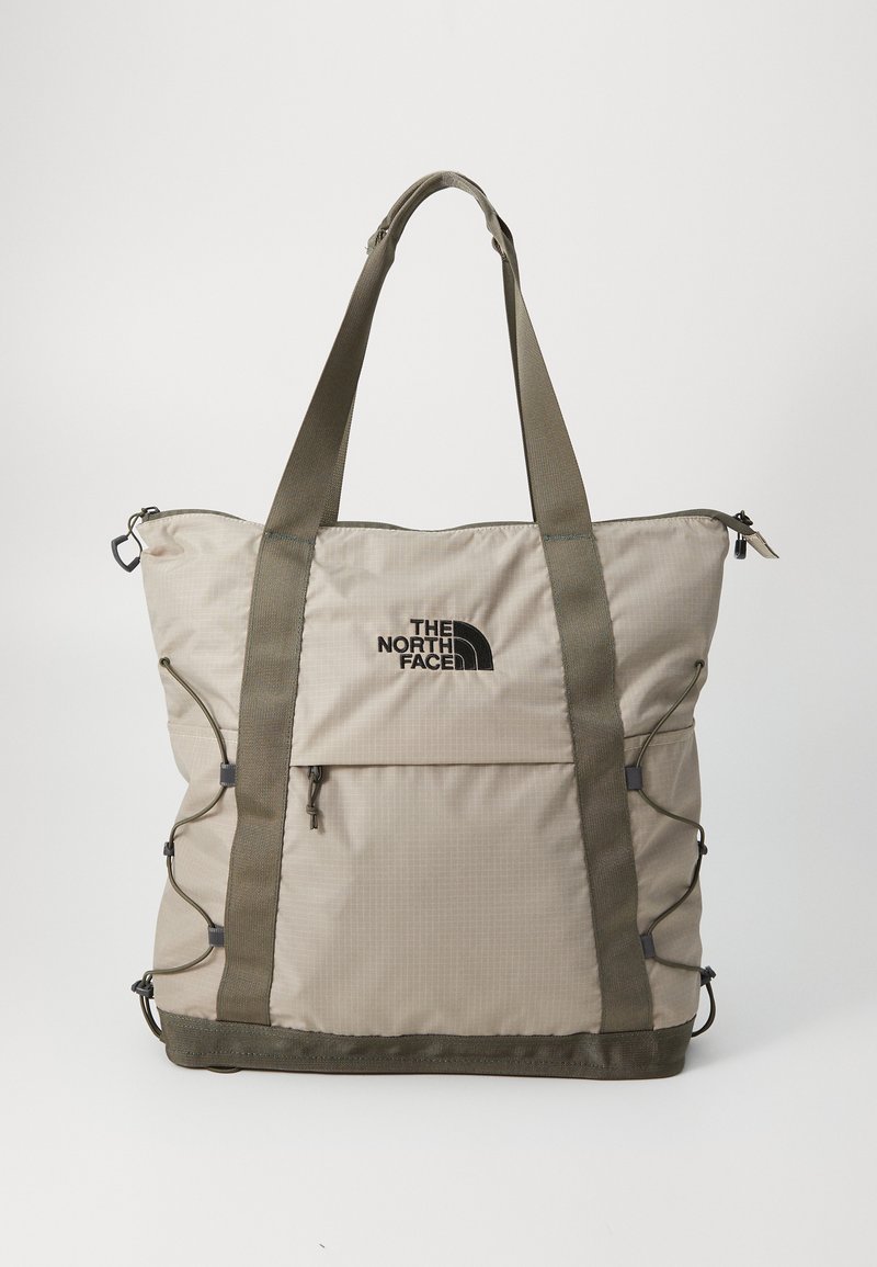 Beige nylon draagtas met olijfgroene handvatten, met een voorste ritszak en logo. Glad textuur met een gestructureerde, vierkante vorm.