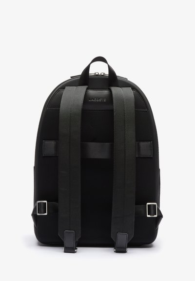 Sac à dos noir en tissu texturé, avec des bretelles rembourrées, de forme rectangulaire et des accents en métal argenté. Il présente un logo sur le devant.