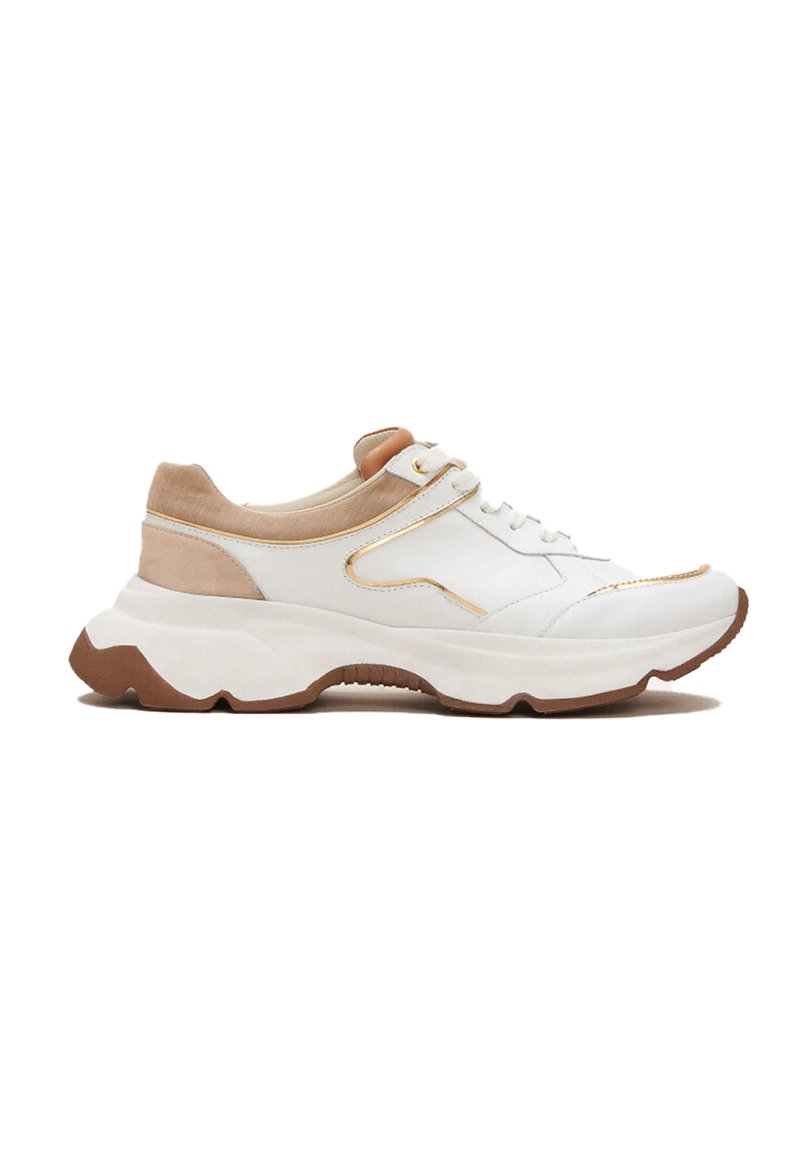 Zapatilla blanca con acentos beige, que presenta una suela gruesa y detalles sutiles en dorado. La parte superior combina texturas de cuero liso y ante.